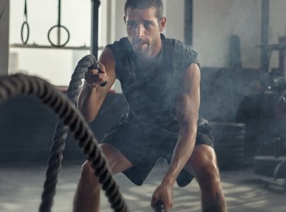 strong young man working out with battle ropes in a crossfit gym