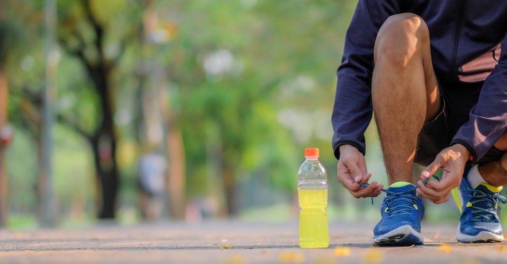 man tying laces with energy drink bottle placed nearby