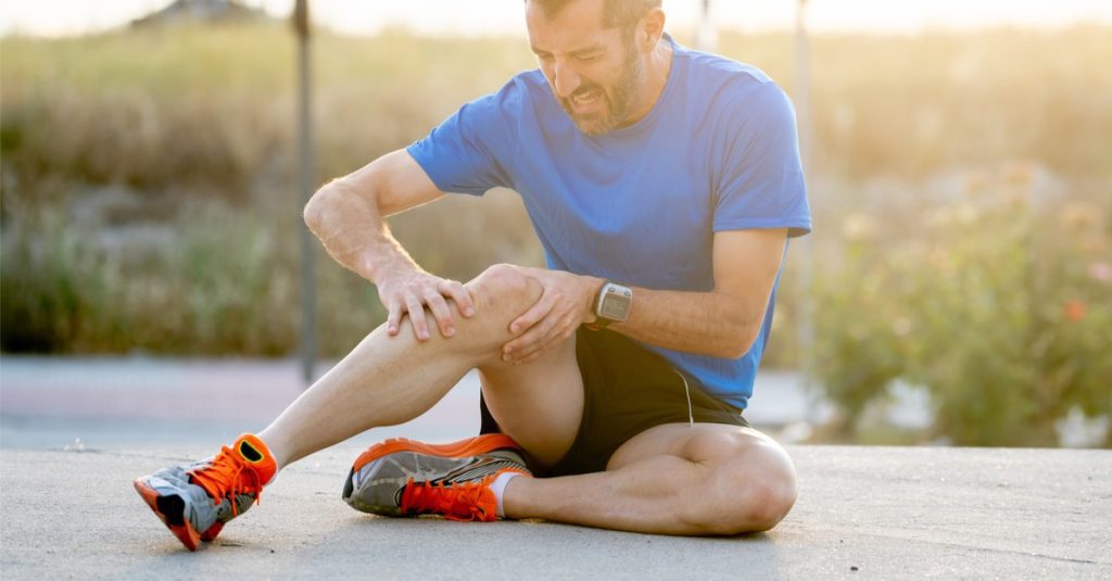 man with strong athletic legs holding knee with his hands in pain