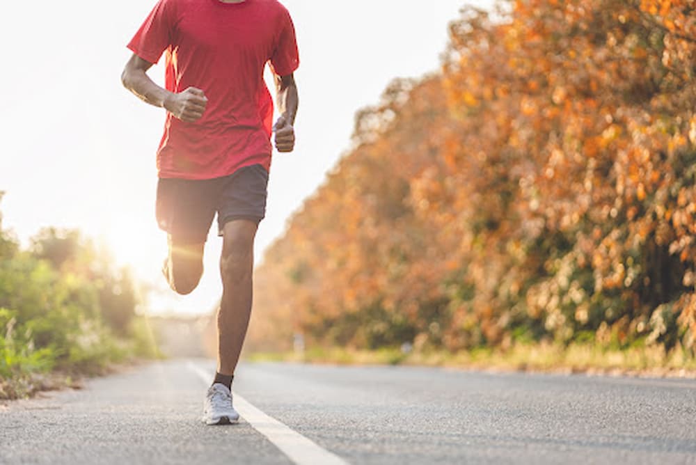 Athletic man running down side of road lined by trees