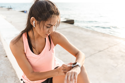 Young woman wearing headphones checking her sports watch while running on pier